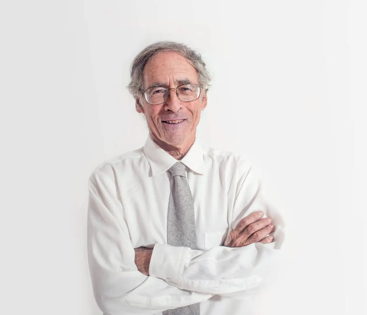 A man with glasses and a tie standing in front of a white wall.
