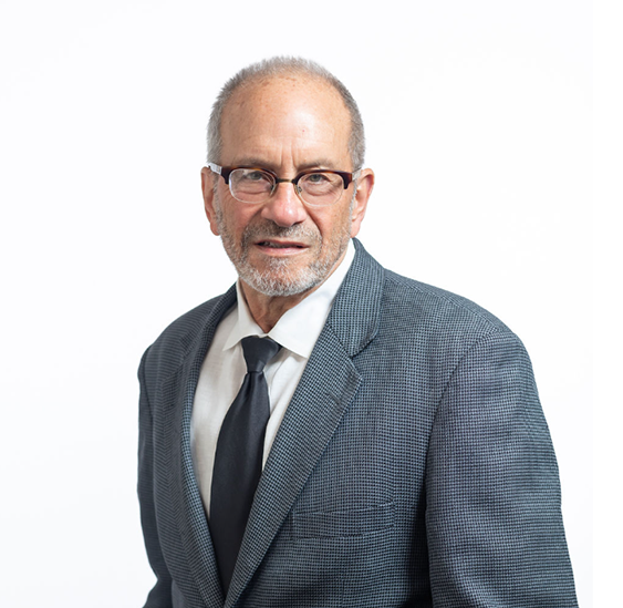 A man in a suit and tie standing up against a white wall.