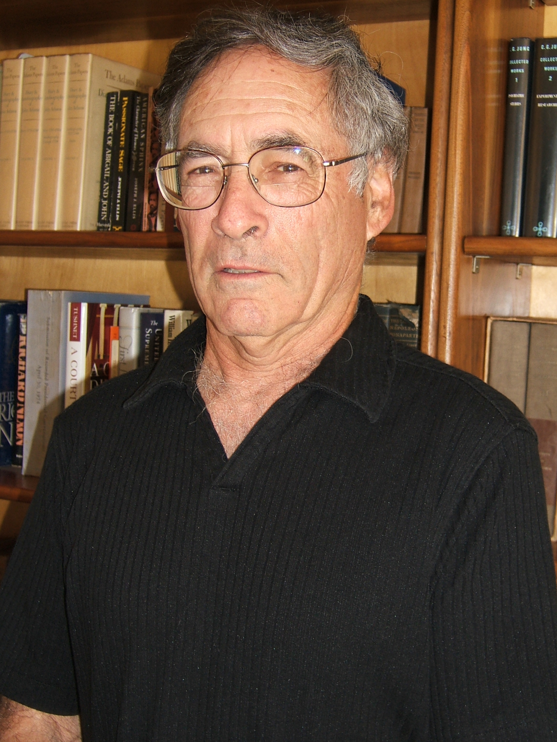 Older man with glasses by bookshelves
